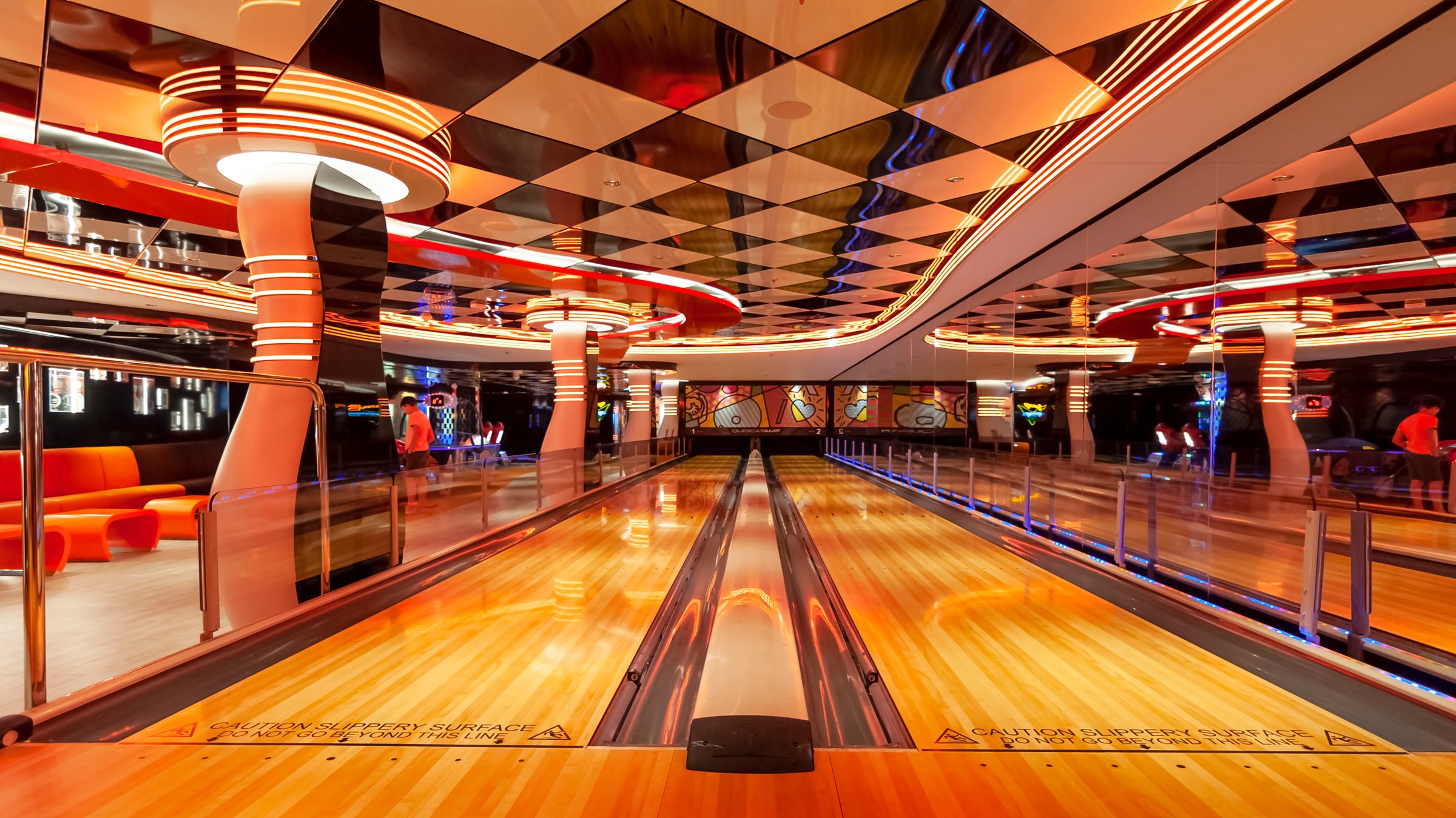 Modern bowling alley with mirrored geometric ceiling, orange and amber LED lighting, two polished wooden lanes, and reflective surfaces creating depth