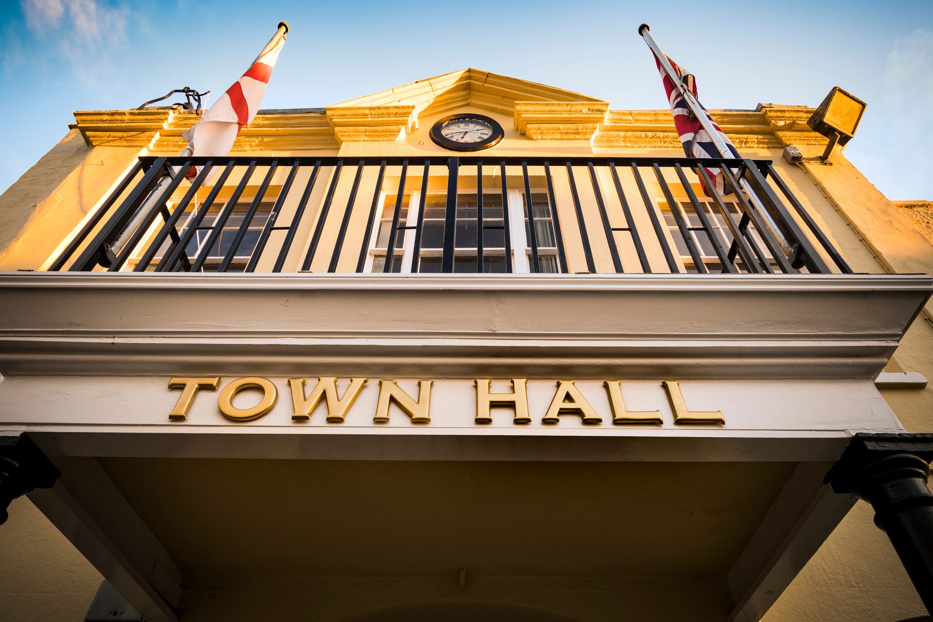 Yellow-painted town hall facade at golden hour, with the Union Jack flag flying, a clock above the entrance, and 'Town Hall' lettering in gold