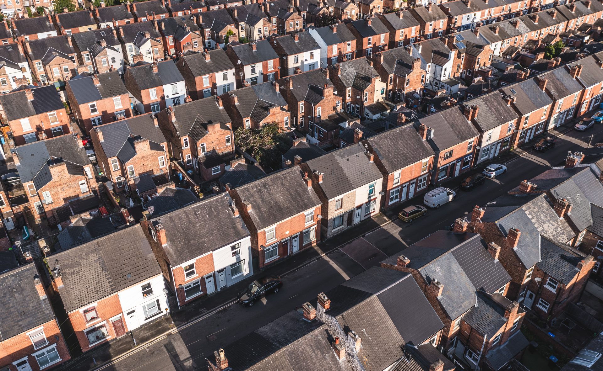 Aerial view of rows of British red-brick terraced housing under a clear sky, conveying the breadth of UK social housing stock